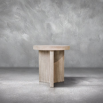 Trinity End Table with a round bleached oak top on a cross-shaped panel base, beside a sofa