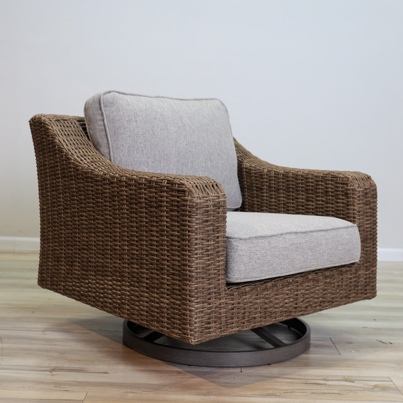 Brown wicker swivel chair with gray cushion on a wooden floor.