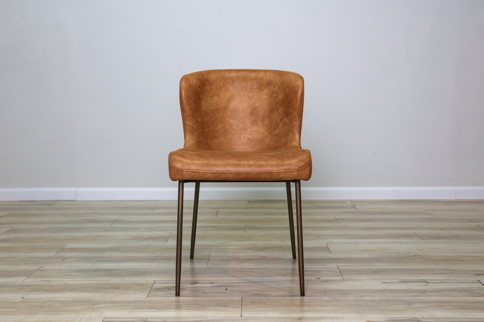 Easley dining chair in cognac brown faux leather with a curved wingback and slim bronze metal legs, dining room