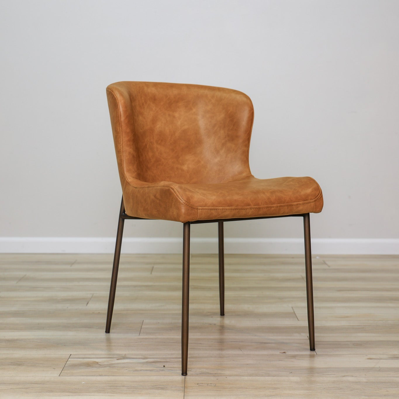 Easley dining chair in cognac brown faux leather with a curved wingback and slim bronze metal legs, dining room