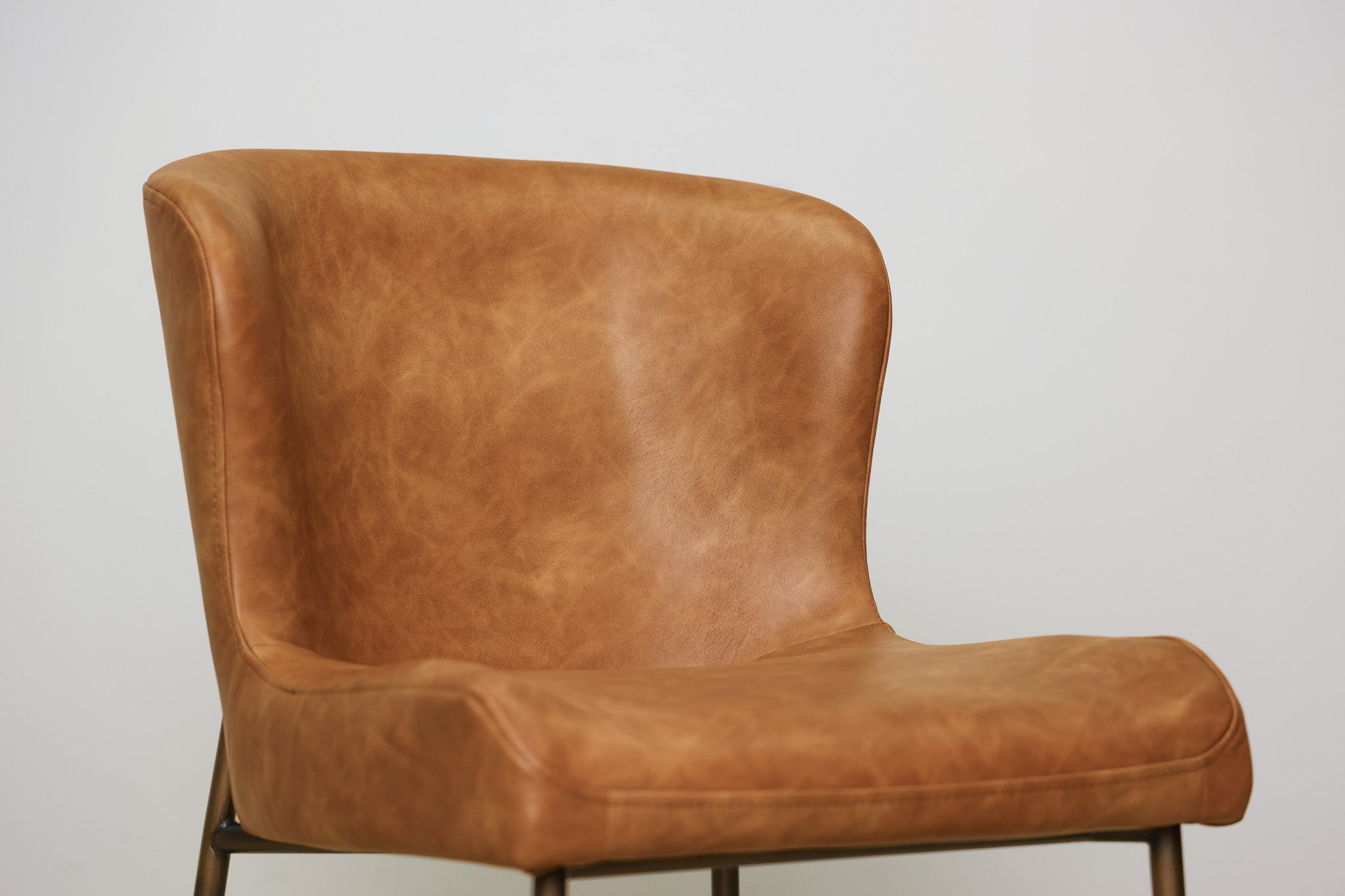 Easley dining chair in cognac brown faux leather with a curved wingback and slim bronze metal legs, dining room