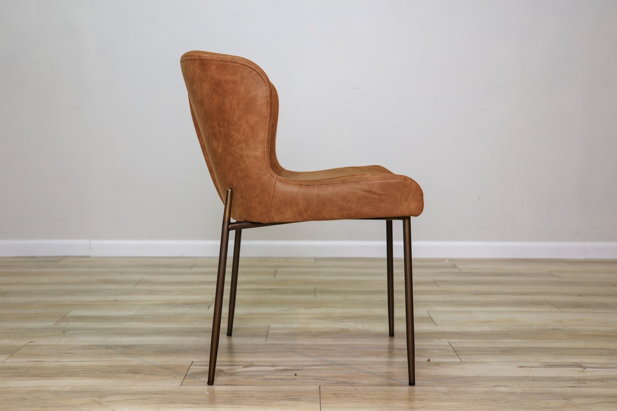 Easley dining chair in cognac brown faux leather with a curved wingback and slim bronze metal legs, dining room