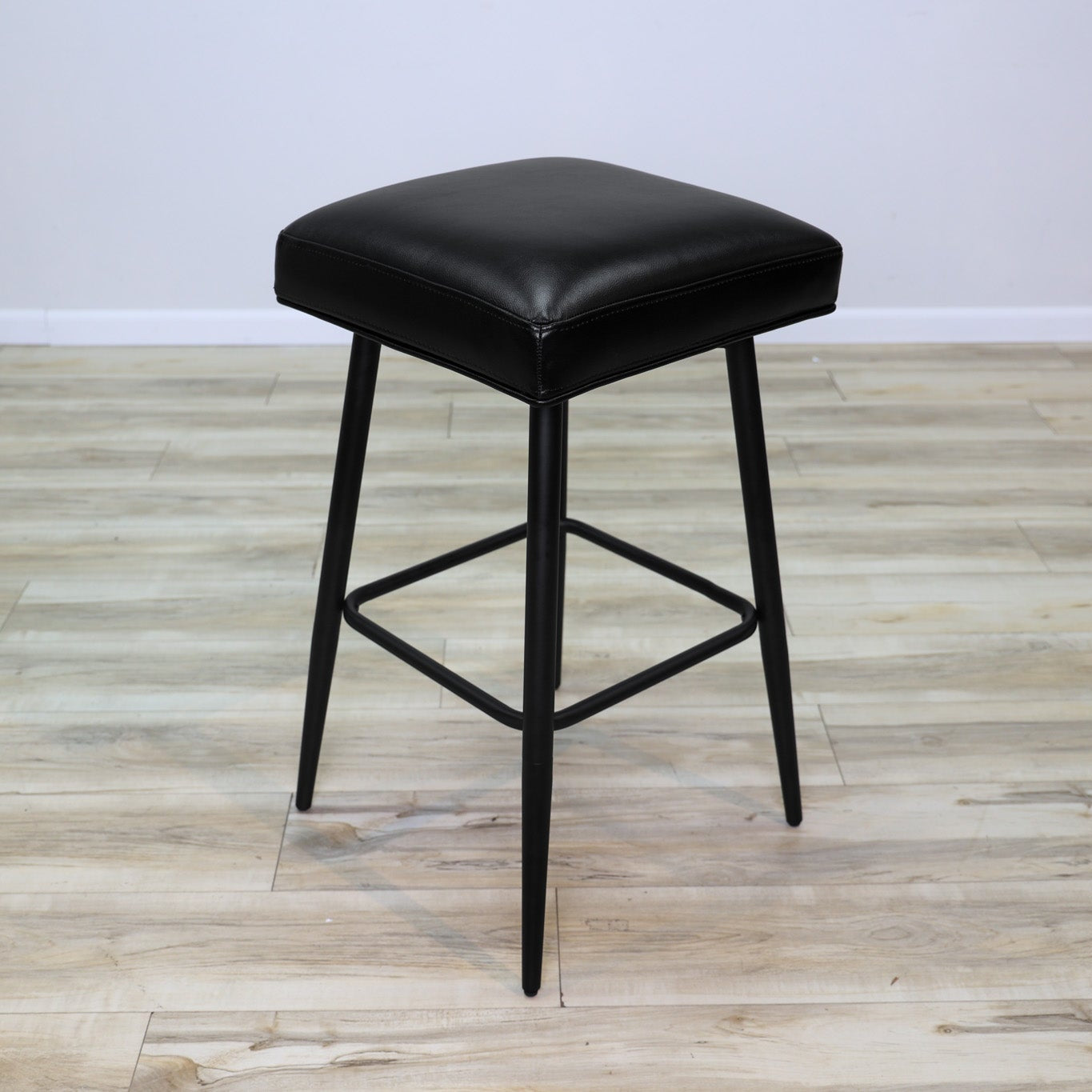 Versa backless adjustable stool in black faux leather with a black metal swivel base and footrest, kitchen bar