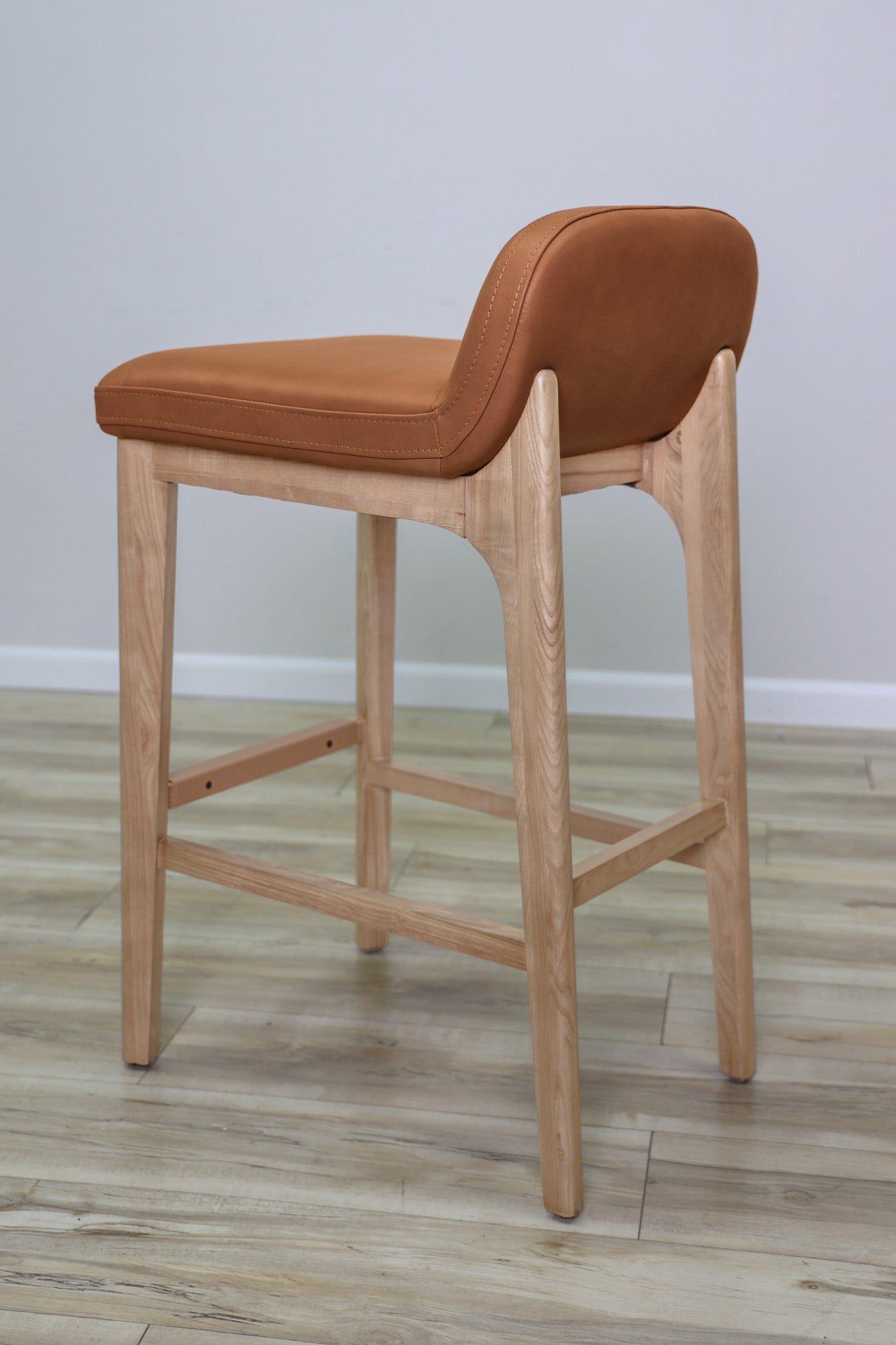 Sable barstool in cognac leather with a low back and natural wood legs with stretchers, kitchen bar