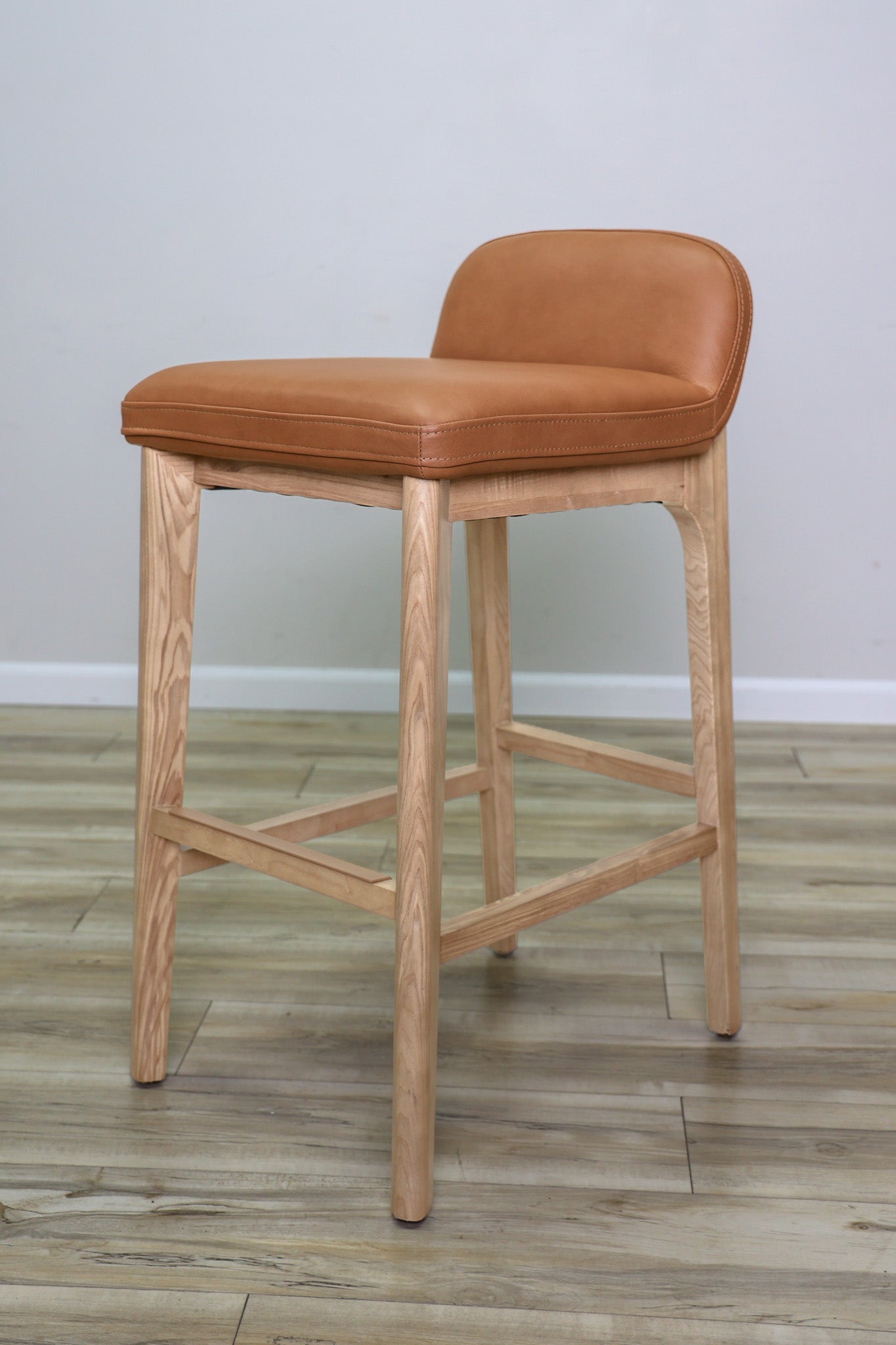 Sable barstool in cognac leather with a low back and natural wood legs with stretchers, kitchen bar