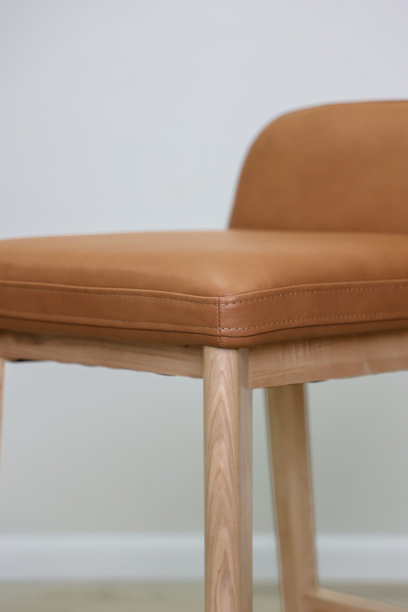 Sable barstool in cognac leather with a low back and natural wood legs with stretchers, kitchen bar
