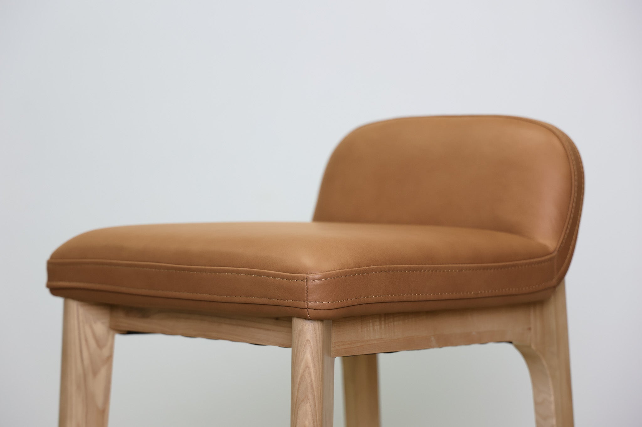 Sable barstool in cognac leather with a low back and natural wood legs with stretchers, kitchen bar