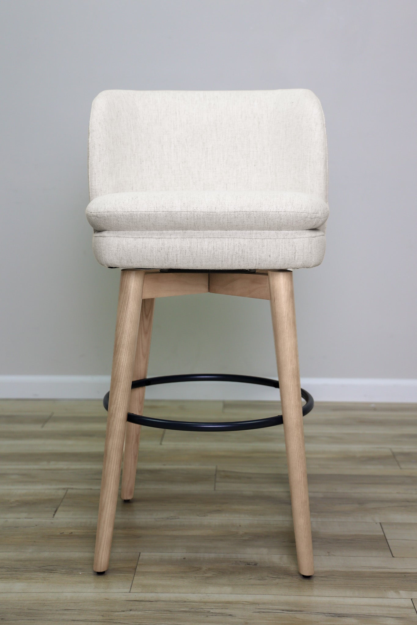 Tiffany swivel barstool in ivory Crypton fabric with natural wood legs and a black ring footrest, kitchen bar