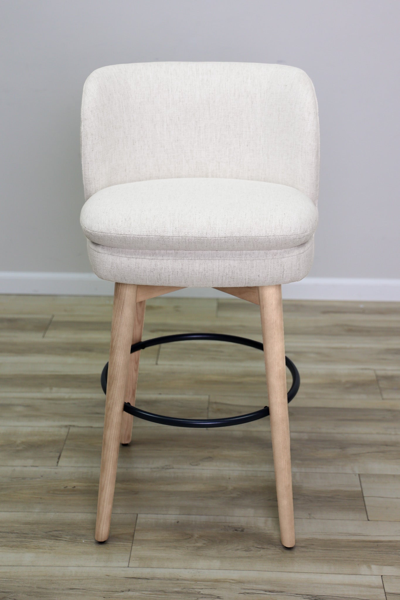Tiffany swivel barstool in ivory Crypton fabric with natural wood legs and a black ring footrest, kitchen bar