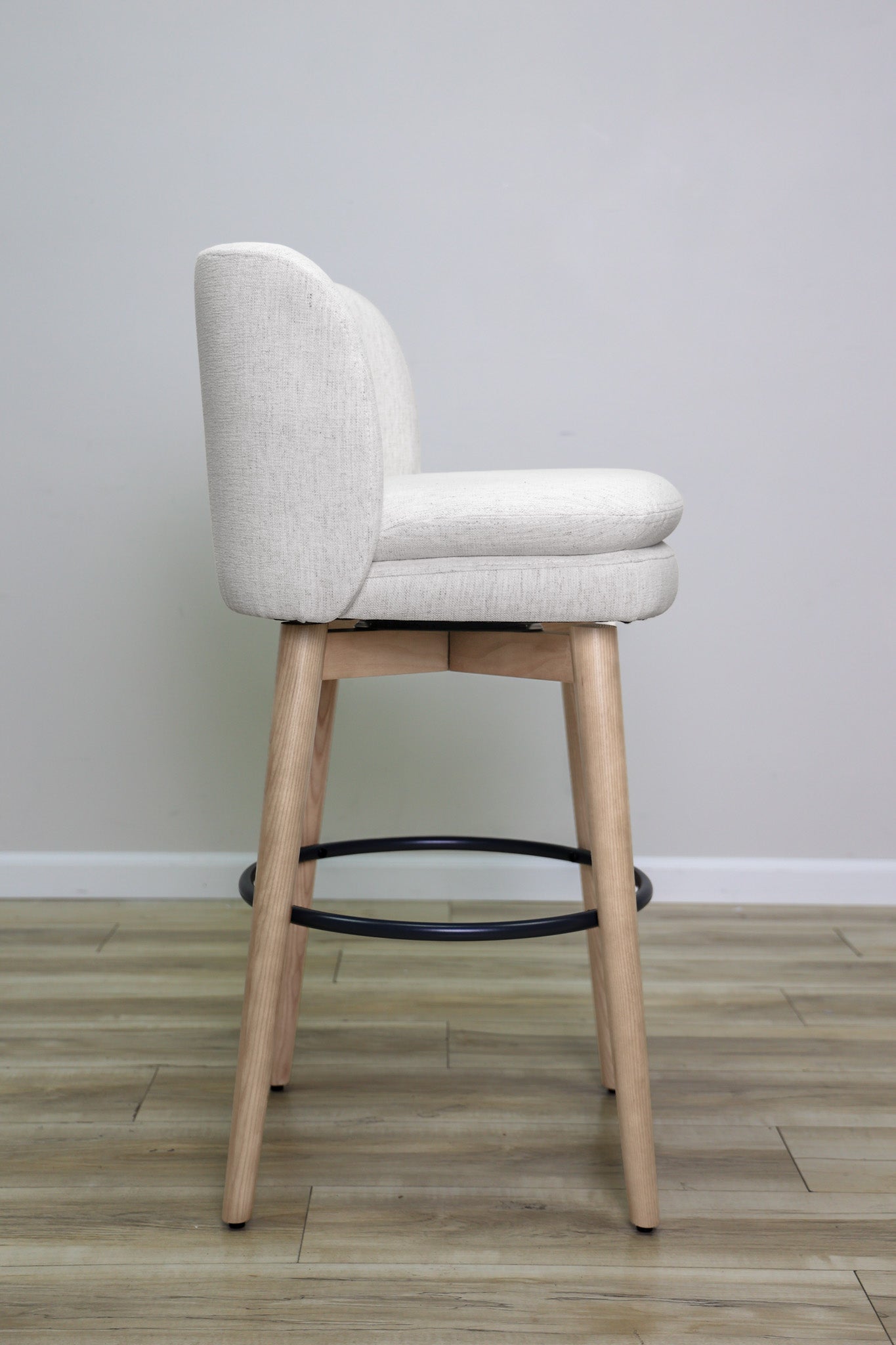 Tiffany swivel barstool in ivory Crypton fabric with natural wood legs and a black ring footrest, kitchen bar