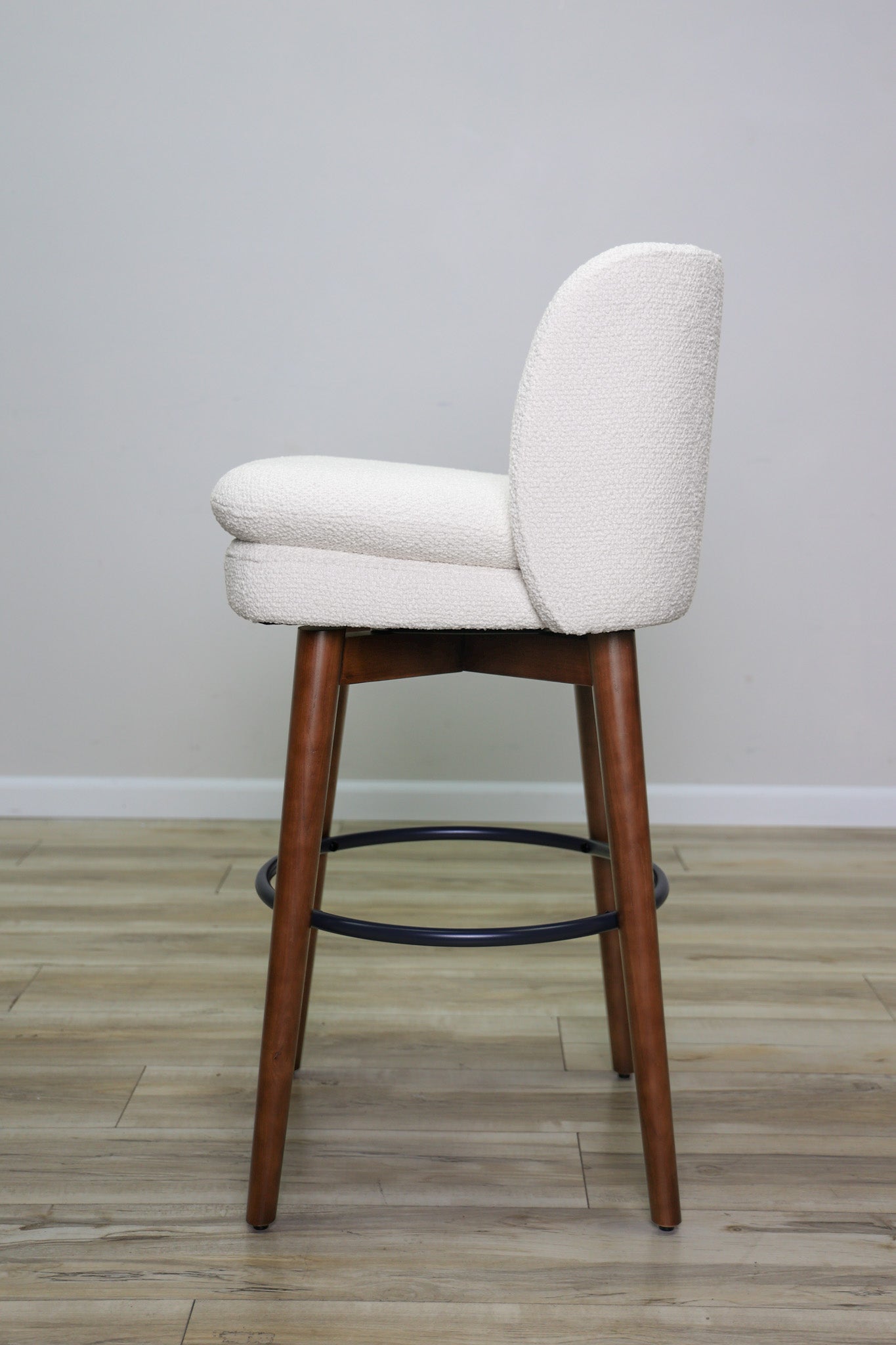 Avalon swivel barstool in cream bouclé performance fabric with walnut wood legs and a black ring footrest, kitchen bar