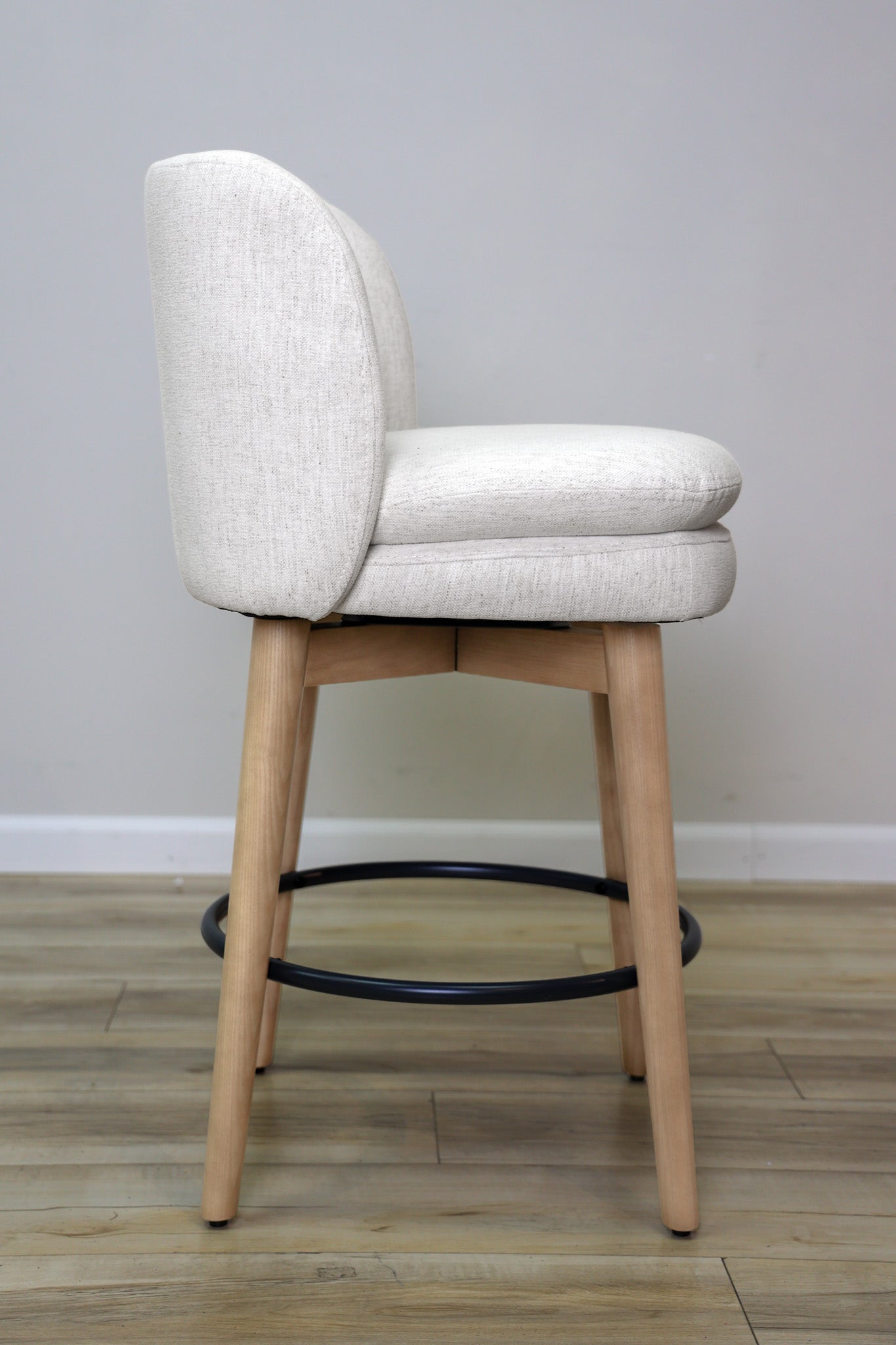 Tiffany swivel counter stool in ivory Crypton fabric with natural wood legs and a black ring footrest, kitchen counter