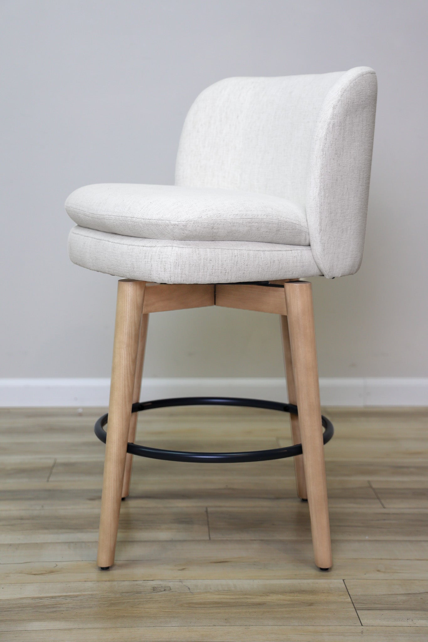 Tiffany swivel counter stool in ivory Crypton fabric with natural wood legs and a black ring footrest, kitchen counter