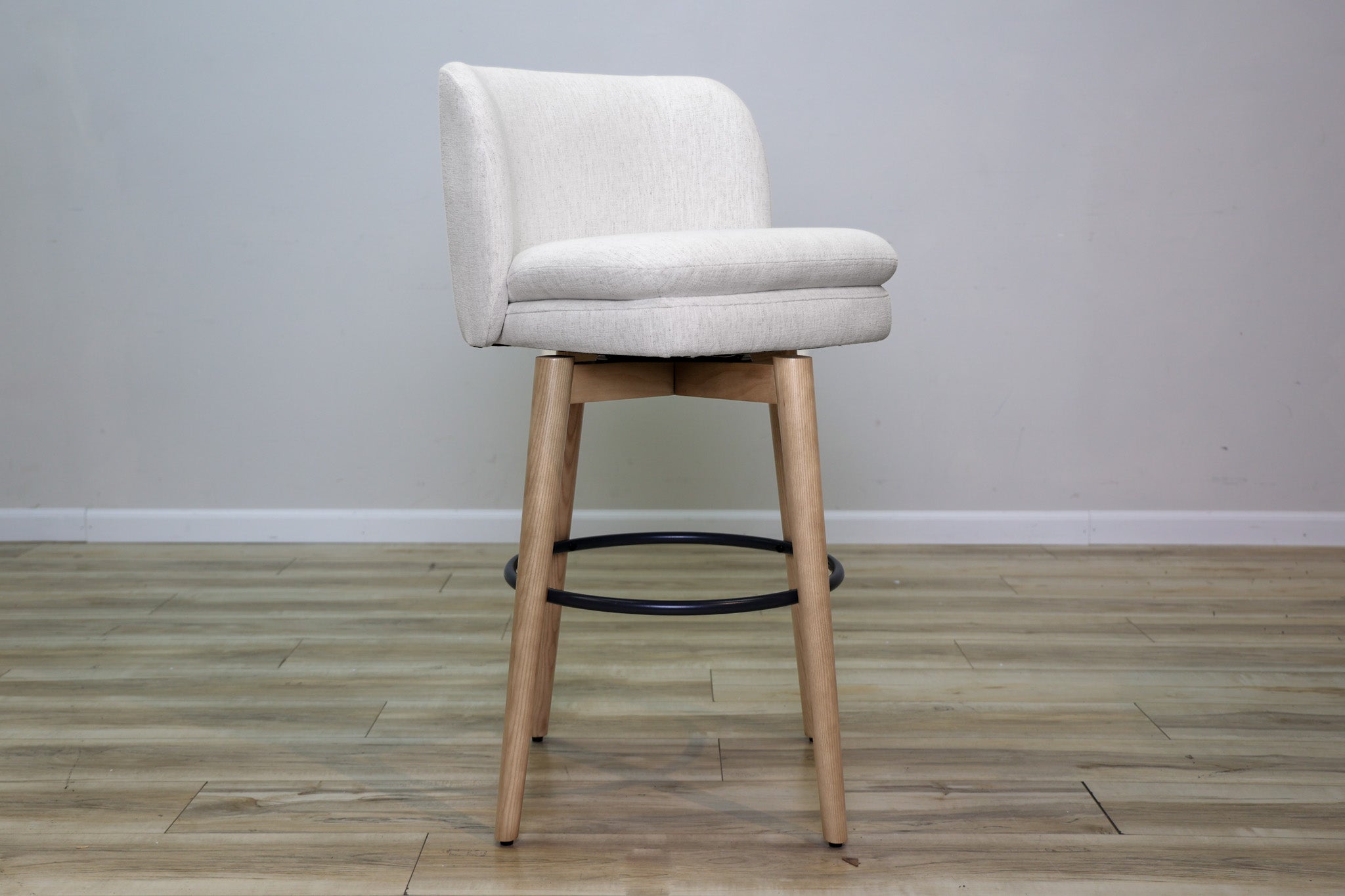 Tiffany swivel barstool in ivory Crypton fabric with natural wood legs and a black ring footrest, kitchen bar