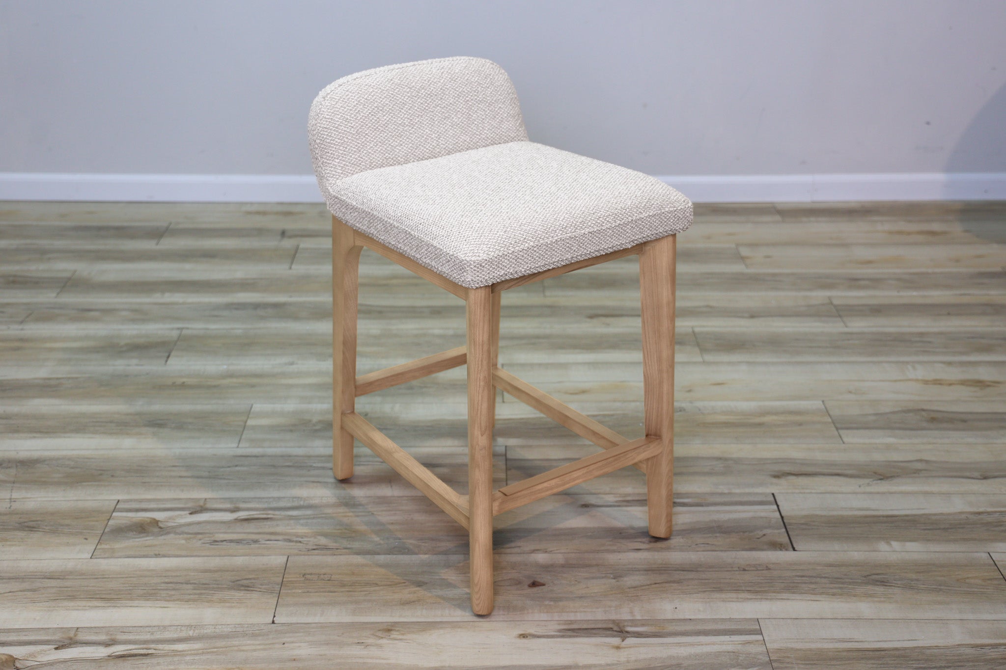 Asher counter stool in beige performance fabric with a low back and natural wood legs with stretchers, kitchen counter