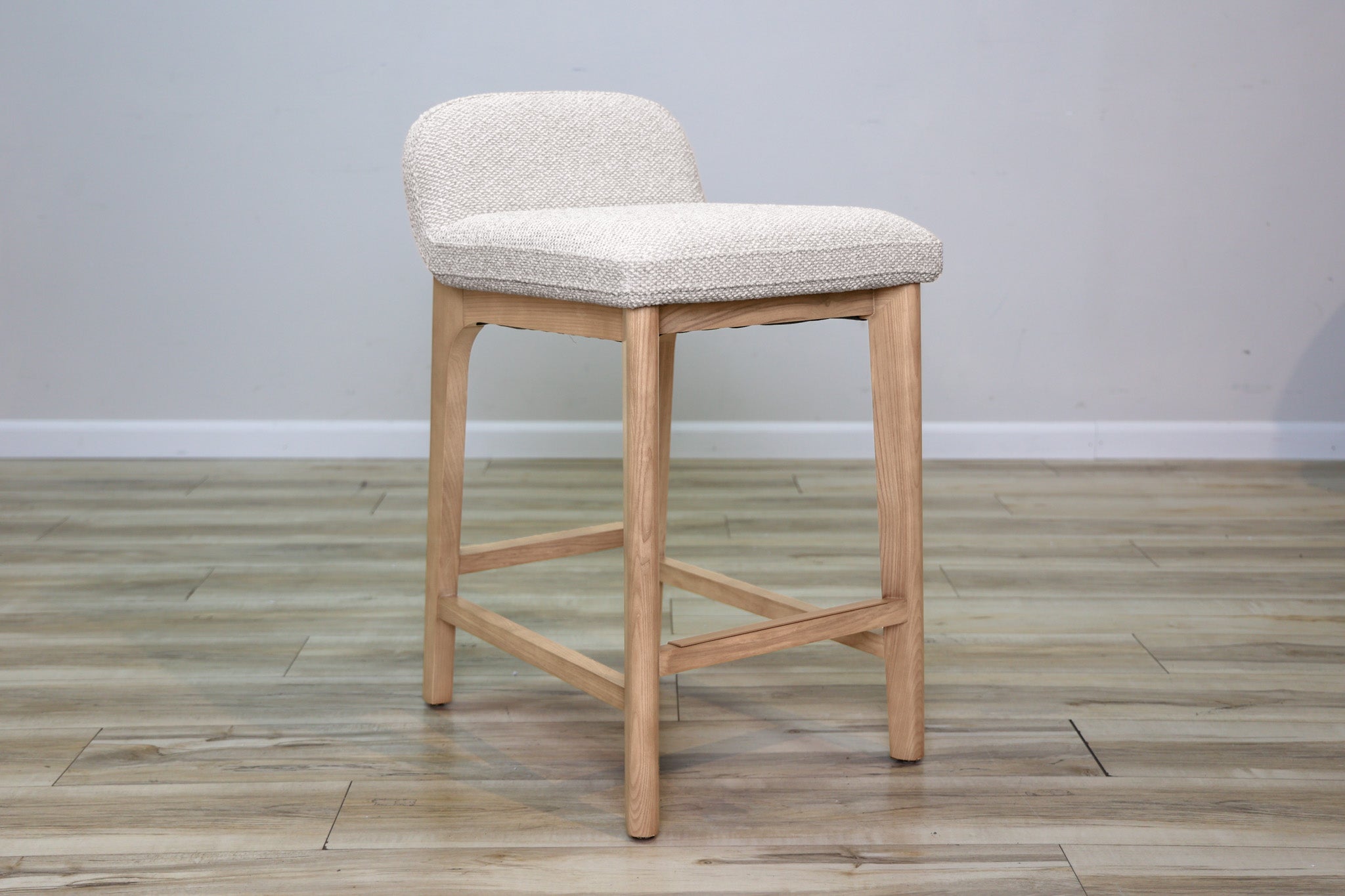 Asher counter stool in beige performance fabric with a low back and natural wood legs with stretchers, kitchen counter