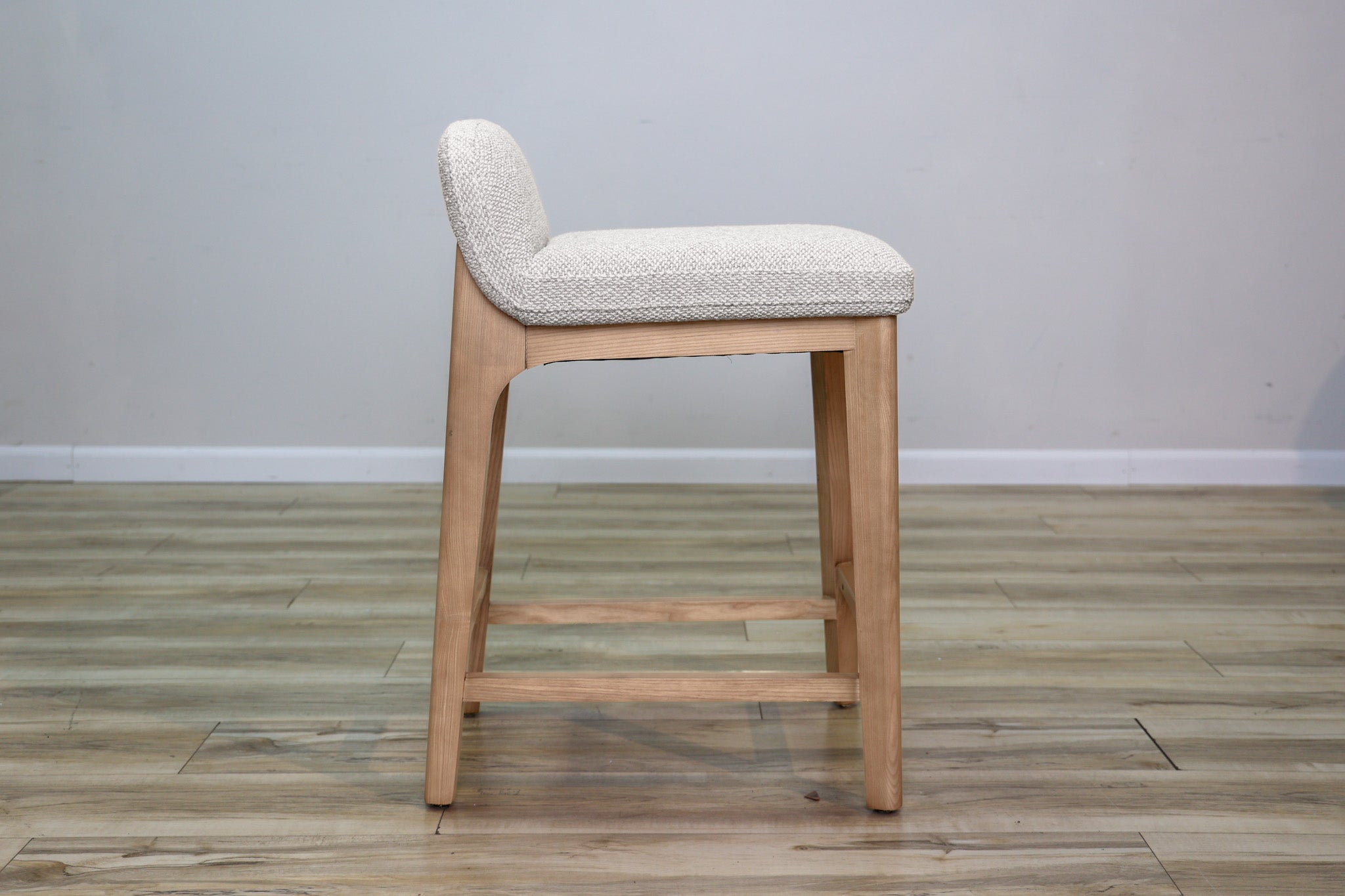 Asher counter stool in beige performance fabric with a low back and natural wood legs with stretchers, kitchen counter