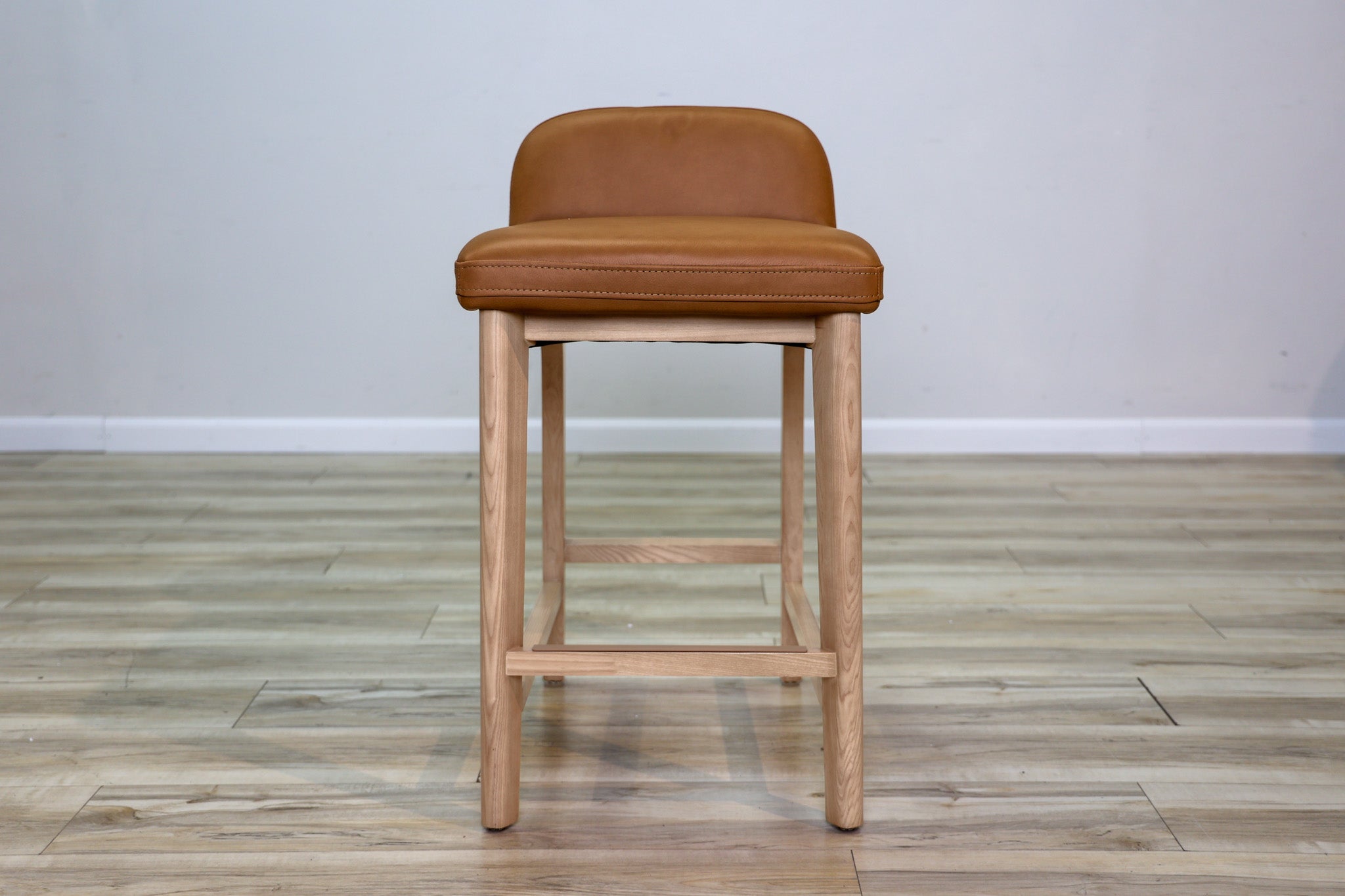 Sable counter stool in cognac leather with a low back and natural wood legs with stretchers, kitchen counter