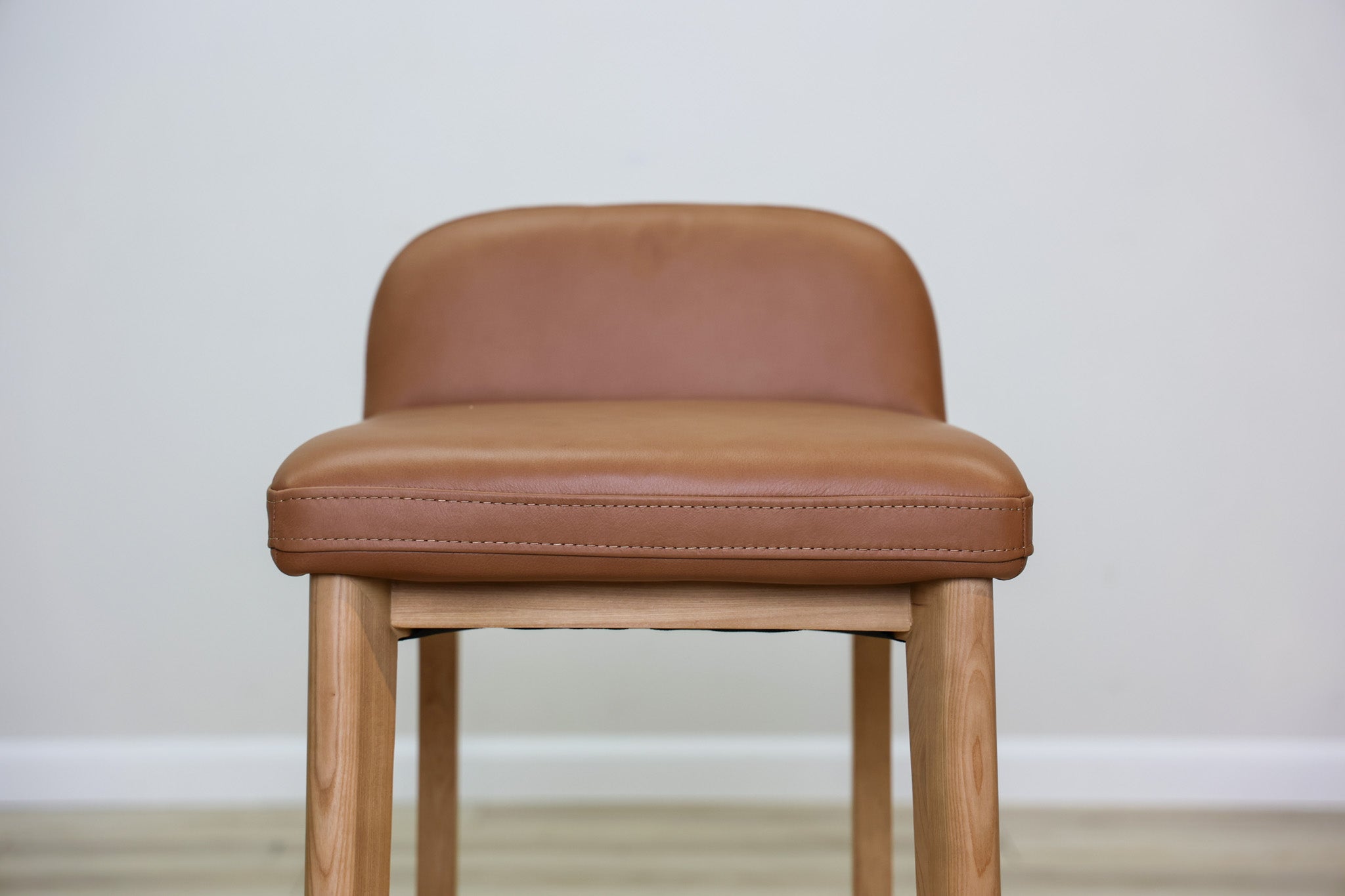 Sable counter stool in cognac leather with a low back and natural wood legs with stretchers, kitchen counter