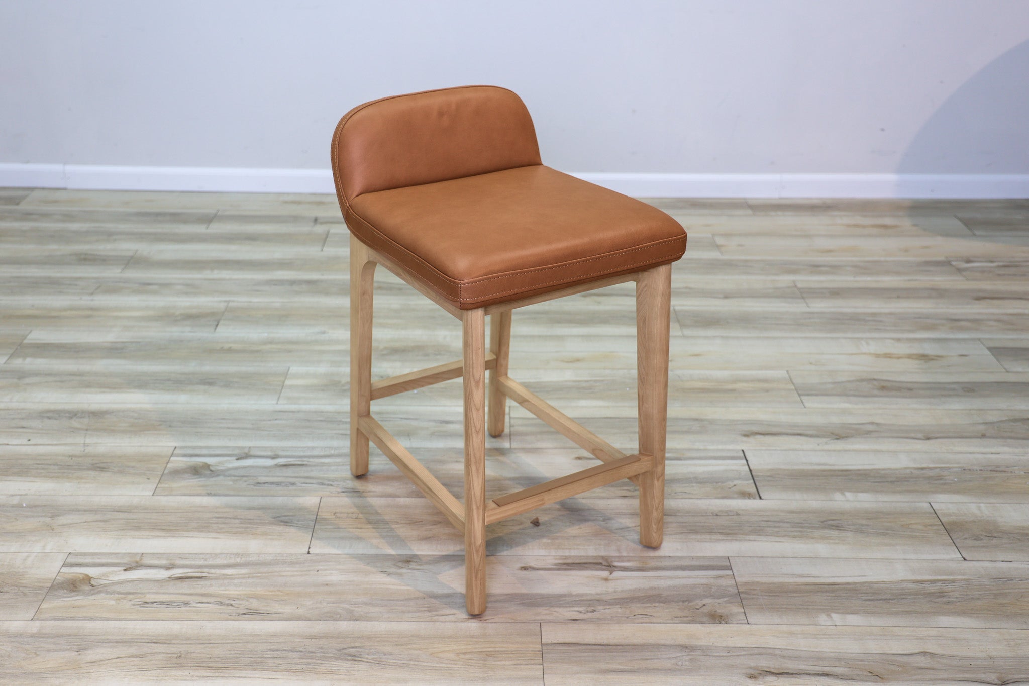 Sable counter stool in cognac leather with a low back and natural wood legs with stretchers, kitchen counter