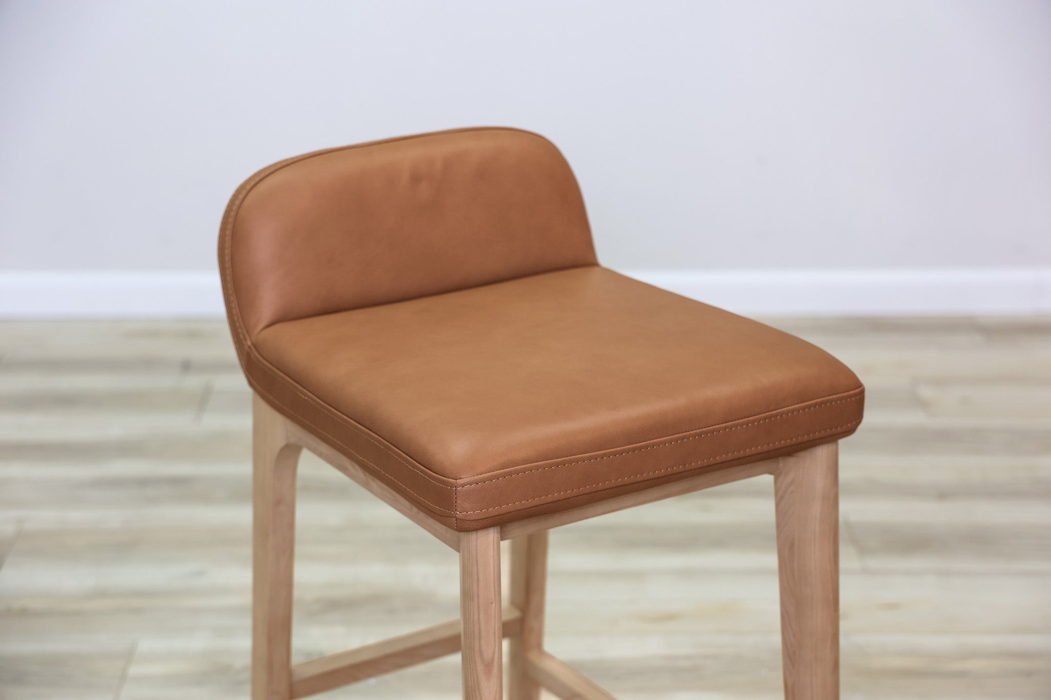 Sable counter stool in cognac leather with a low back and natural wood legs with stretchers, kitchen counter