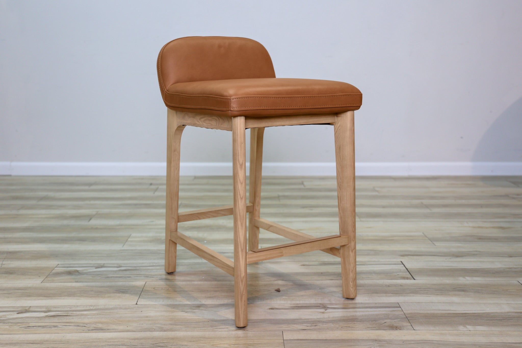 Sable counter stool in cognac leather with a low back and natural wood legs with stretchers, kitchen counter