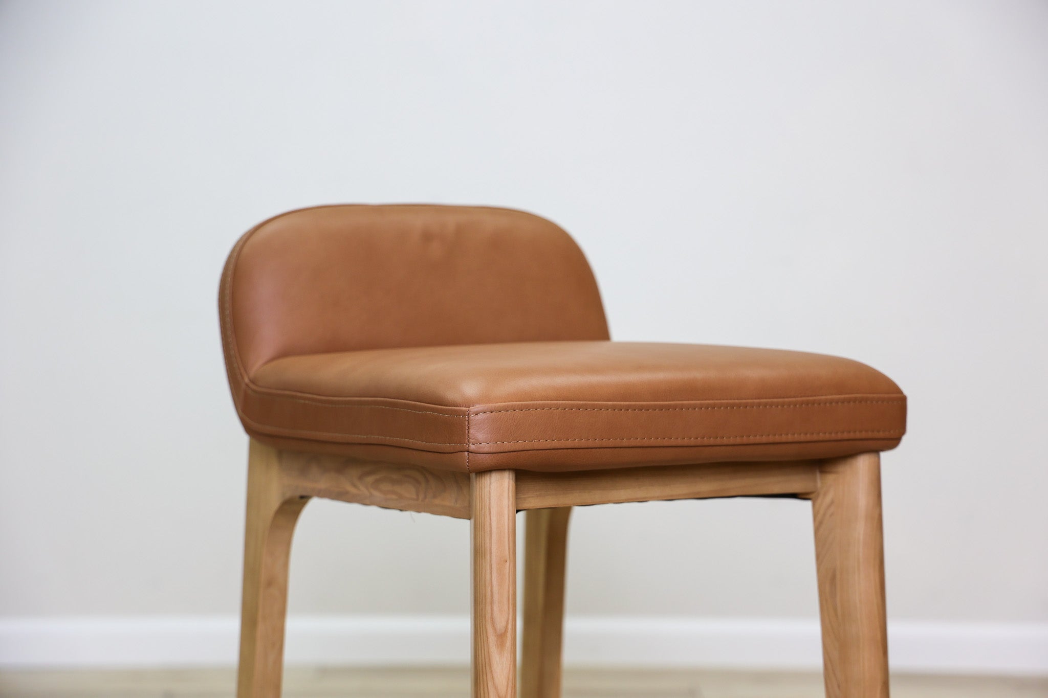 Sable counter stool in cognac leather with a low back and natural wood legs with stretchers, kitchen counter