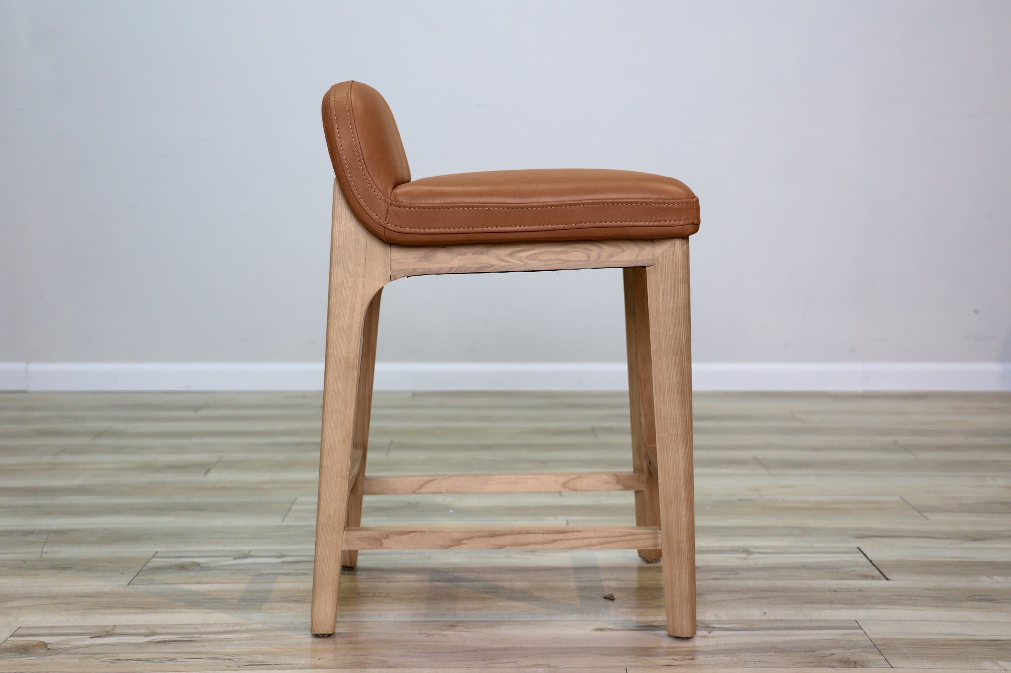 Sable counter stool in cognac leather with a low back and natural wood legs with stretchers, kitchen counter