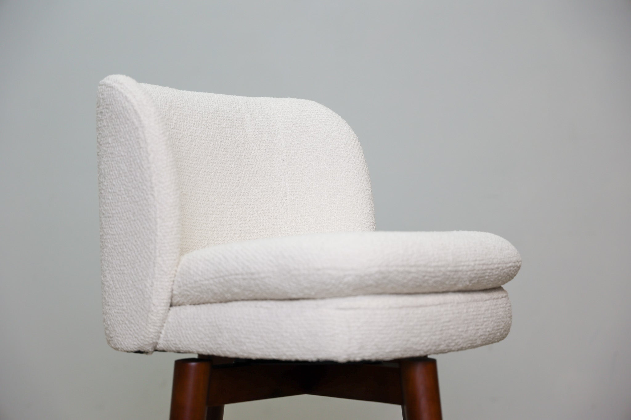 Avalon swivel counter stool in cream bouclé performance fabric with walnut wood legs and a black ring footrest, kitchen counter
