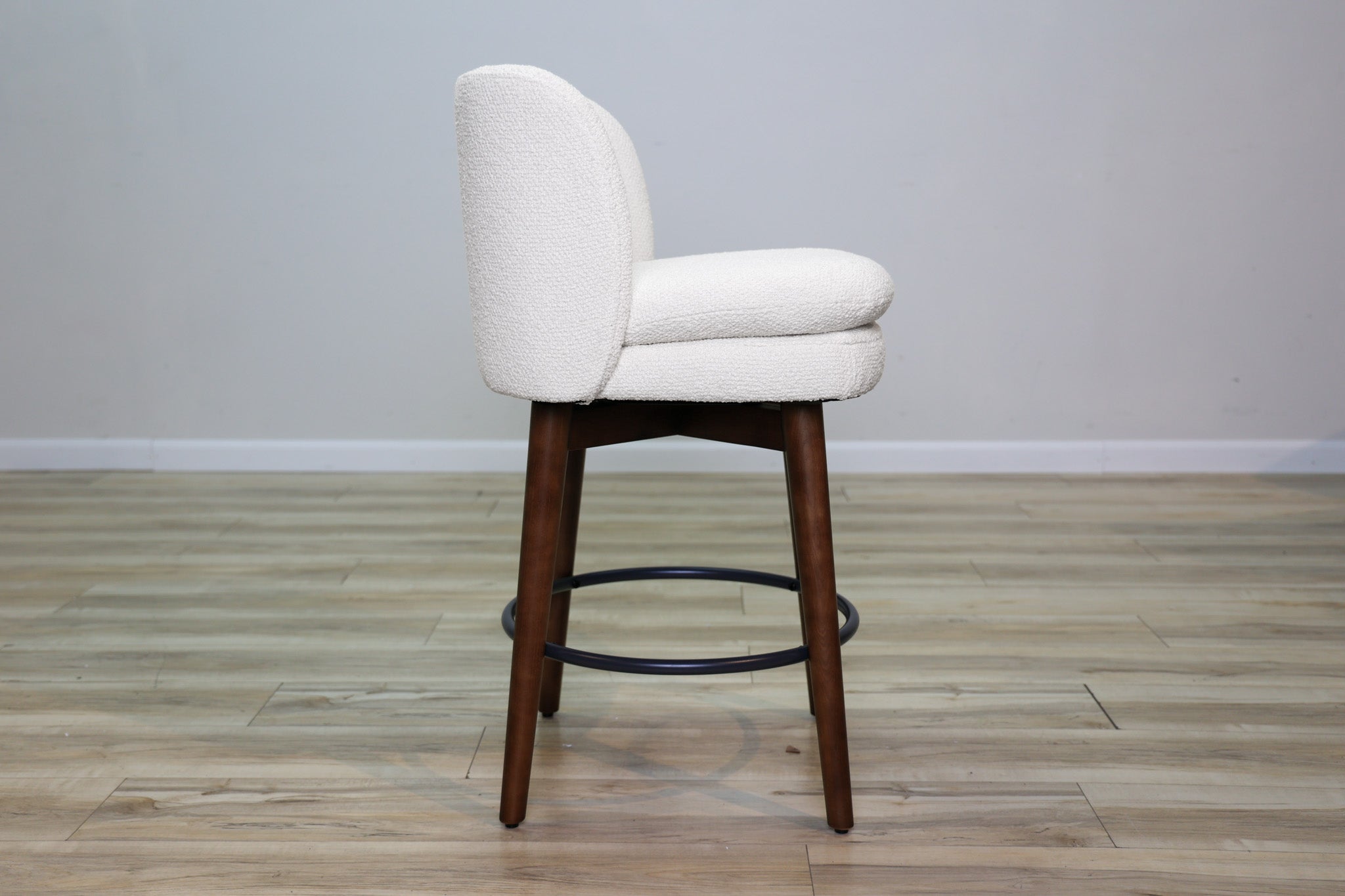 Avalon swivel counter stool in cream bouclé performance fabric with walnut wood legs and a black ring footrest, kitchen counter