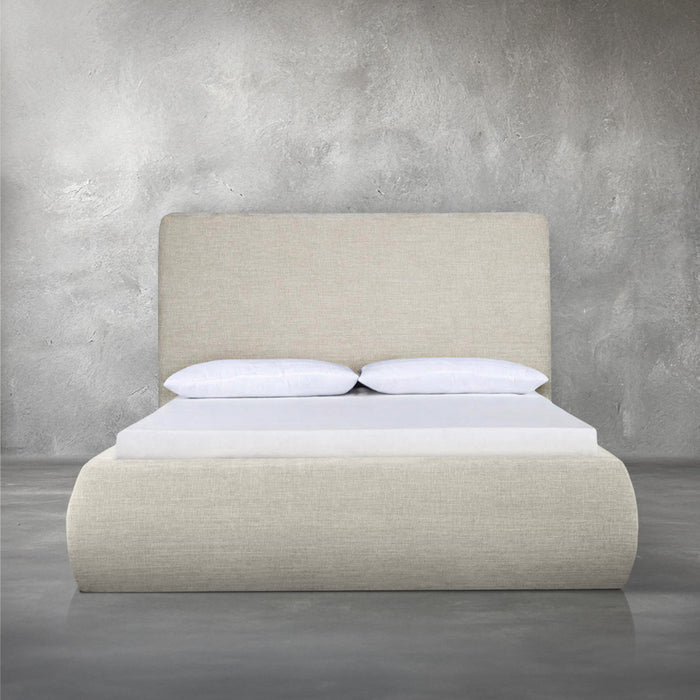 Bain Bed, a fully upholstered platform bed in warm beige performance fabric with a rounded headboard and a softly curved, floor-grazing base