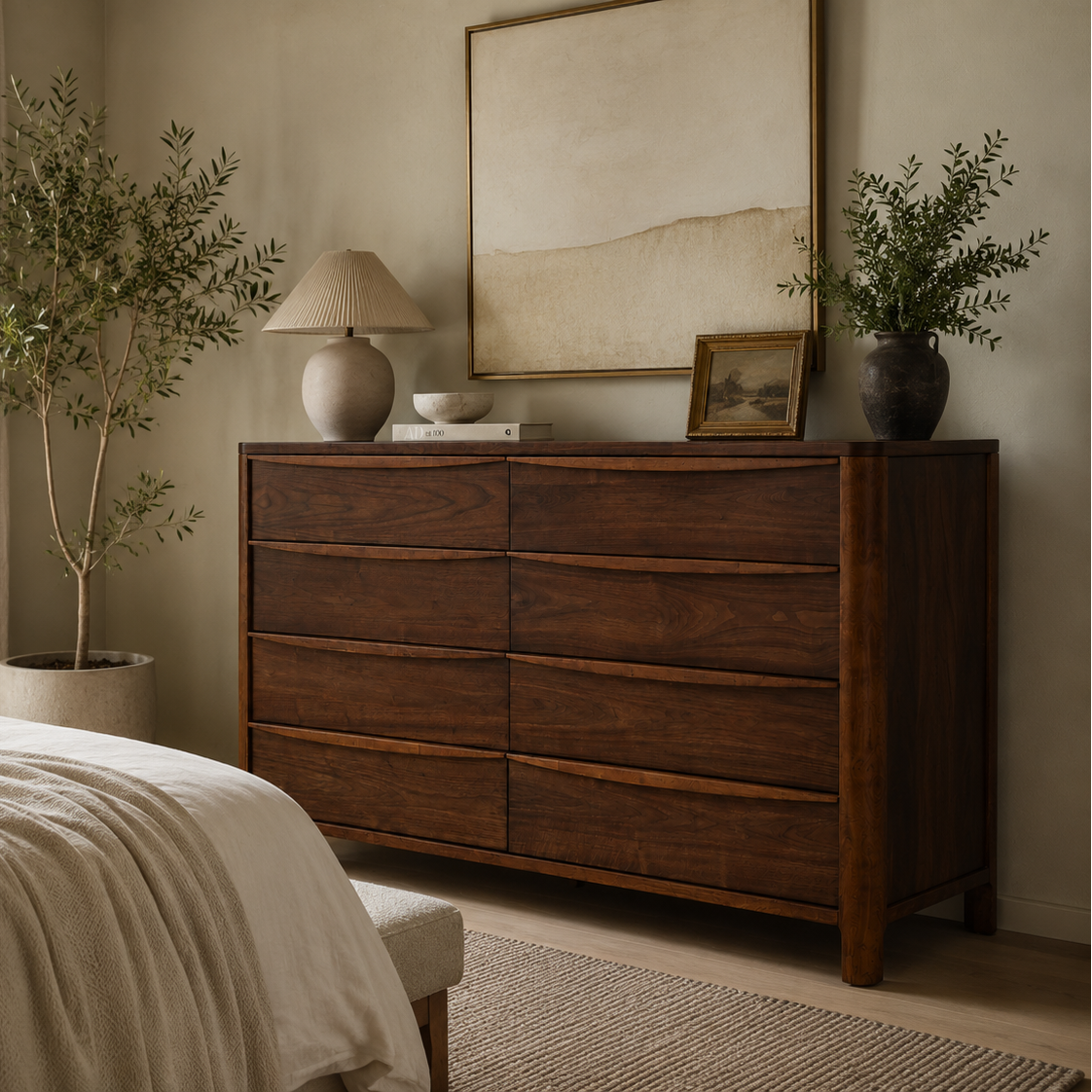 A dark brown wooden six-drawer dresser in a beautifully styled bedroom, topped with a beige table lamp, a small framed picture, and a vase with greenery.