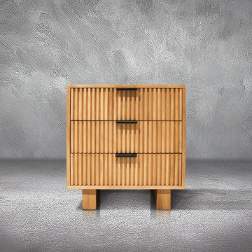 Fluted Nightstand in natural mango wood with hand-carved fluted drawers and splayed feet, beside a bed
