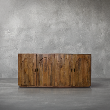Raye Credenza in natural mango wood with arched carved door fronts and gold hardware, in a living room